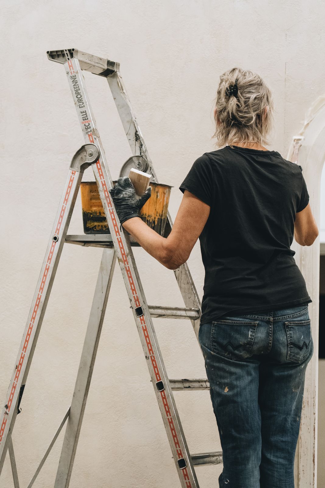 Une peintre sur un escabeau, pot de peinture à la main